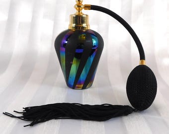 May include: A vintage perfume bottle with a black, iridescent glass body and gold-colored accents. The bottle features a black bulb atomizer and a long black tassel. The design includes diagonal stripes with rainbow-colored reflections.