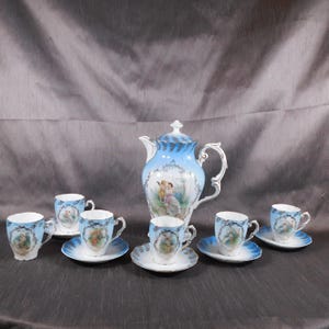 Op de afbeelding: Een vintage porseleinen theeservies met een blauw en wit bloemenmotief. De set bevat een theepot, zes kopjes en zes schoteltjes. De kopjes en schoteltjes tonen een romantische scène van een stel in een tuin.