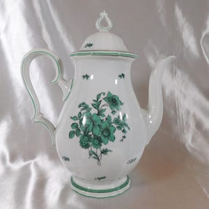 May include: White porcelain coffee pot with a lid, featuring a green floral design. The pot has a curved handle and spout, with green trim. The design includes a bouquet of flowers and decorative accents.