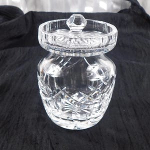 Könnte beinhalten: Ein klarer, geschliffener Glasbehälter mit Deckel. Der Behälter hat einen abgerundeten Körper und eine breite, kreisförmige Öffnung. Der Deckel ist ebenfalls aus geschliffenem Glas und hat einen kleinen, facettierten Knopf. Der Behälter ist mit einem Diamanten- und Sternmuster verziert.