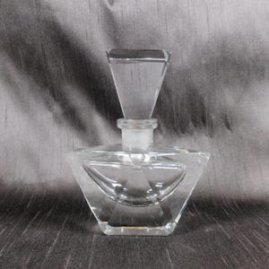 May include: A clear glass perfume bottle with a geometric design. The bottle has a square base and a triangular top.