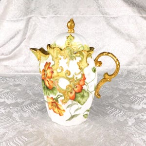 May include: A white porcelain teapot featuring a hand-painted floral pattern of orange and yellow nasturtium flowers with green leaves. The teapot is adorned with ornate, raised gold-colored scrollwork detailing on the lid, spout, and handle.