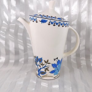 May include: A white ceramic coffee pot with a lid, featuring a blue floral design. The pot has a curved handle and a spout. The floral pattern includes blue flowers and brown leaves. The lid has a matching blue and brown border.