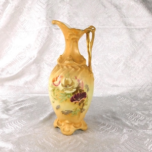 Pode incluir: Um jarro de cerâmica amarela com uma asa curva e um bico alargado. O corpo do jarro é decorado com um motivo floral pintado que apresenta flores brancas, roxas e cor de laranja com folhas verdes sobre um fundo amarelo suave.