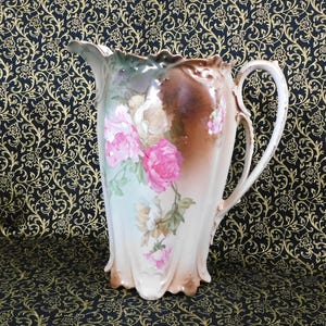 May include: A vintage porcelain pitcher with a floral design. The pitcher is white with a brown glaze and features pink and white roses with green leaves.