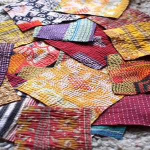 May include: A collection of colorful, quilted fabric patches in various shapes and sizes. The patches feature a variety of patterns, including geometric designs, stripes, and floral motifs. The color palette includes red, yellow, purple, and blue.