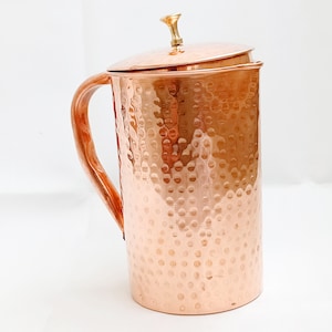 May include: A hammered copper pitcher with a brass lid. The pitcher has a handle and a hammered texture.