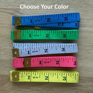 May include: Five measuring tapes in different colors: blue, green, white, pink, and yellow. Each tape is marked with inches and has a metal end cap.