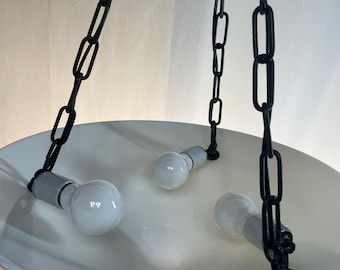 May include: A white, bowl-shaped pendant light fixture with three exposed light bulbs. The fixture is suspended by black chains. The light bulbs are white and the fixture has a glossy finish. The chains are attached to the ceiling.
