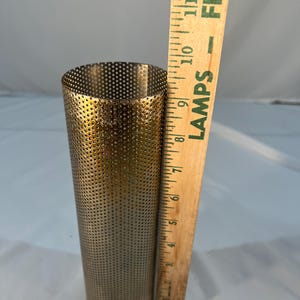 May include: A cylindrical, perforated metal tube in a brass color. The tube is approximately 8 inches tall and has numerous small holes. A wooden ruler is placed next to the tube for scale.