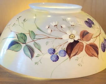 May include: A glass lampshade with a hand-painted floral design. The shade is a soft yellow with a white rim and features green leaves, brown leaves, white flowers, and purple berries. The overall shape is rounded.