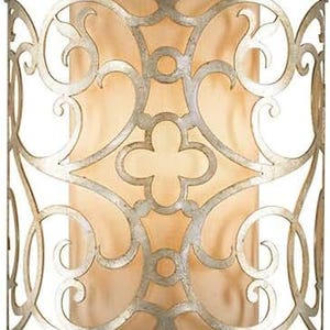May include: A decorative wall sconce with a silver finish and an intricate, openwork design. The metalwork features scrolling patterns and a central quatrefoil motif, surrounding a soft, beige shade. The sconce has a cylindrical shape and is designed for indoor lighting.
