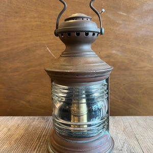 Puede incluir: Linterna antigua de cobre con lente de vidrio transparente y acanalado. La linterna tiene un asa en la parte superior y una base redonda. El metal tiene una pátina desgastada. Una lámpara náutica vintage.
