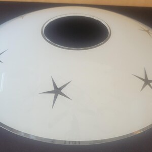 May include: White, oval-shaped mid-century modern ceiling light fixture with a black center opening and silver trim. The fixture features three black starburst designs. A stylish lighting element for any room.