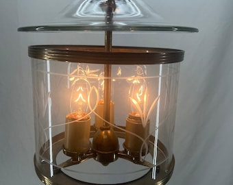 Puede incluir: Una lámpara colgante de tres luces de latón y vidrio con una pantalla de vidrio transparente y un diseño grabado. La lámpara está colgada de una cadena.