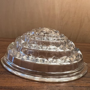 May include: Clear glass decorative bowl with a tiered, geometric design. The bowl has a wide, shallow base and a series of concentric, diamond-shaped tiers leading to a central peak. The glass is transparent, allowing light to pass through.