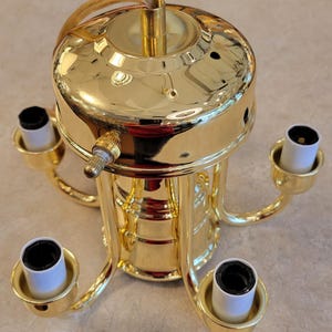 May include: A gold-colored, multi-light ceiling fixture with four curved arms, each holding a white and black light socket. The fixture has a central cylindrical body and a top plate with a wire and a switch.