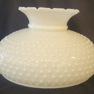 May include: A white milk glass lamp shade featuring a raised hobnail texture across its rounded body. The shade has a wide, flared opening at the top with a scalloped, ruffled edge, and a smooth, circular base designed for attachment to a lamp fixture.