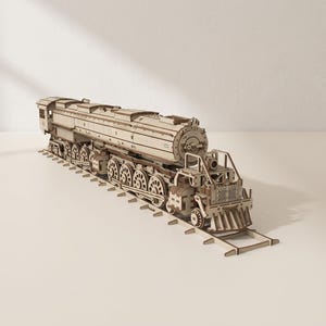 May include: A light brown wooden model train locomotive featuring intricate mechanical details, multiple wheels, and a cowcatcher at the front. The train is positioned on a matching wooden track section, showcasing a complex assembly of interlocking parts.