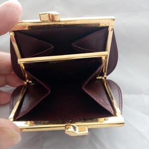 May include: A small, burgundy leather coin purse with a gold metal frame and clasp. The purse is open and the inside is visible. The purse has two compartments.