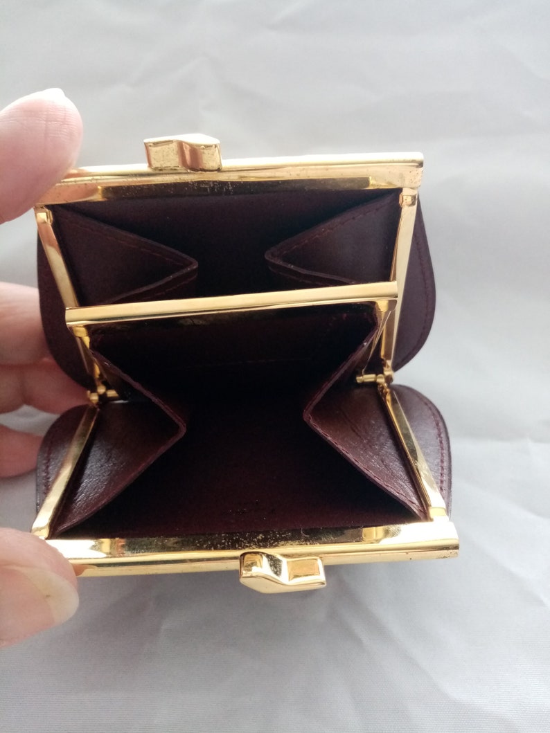 May include: A small, burgundy leather coin purse with a gold metal frame and clasp. The purse is open and the inside is visible. The purse has two compartments.