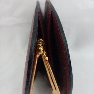 May include: A close-up of a burgundy leather wallet with a gold clasp. The wallet is folded in half and the clasp is visible in the center of the image.