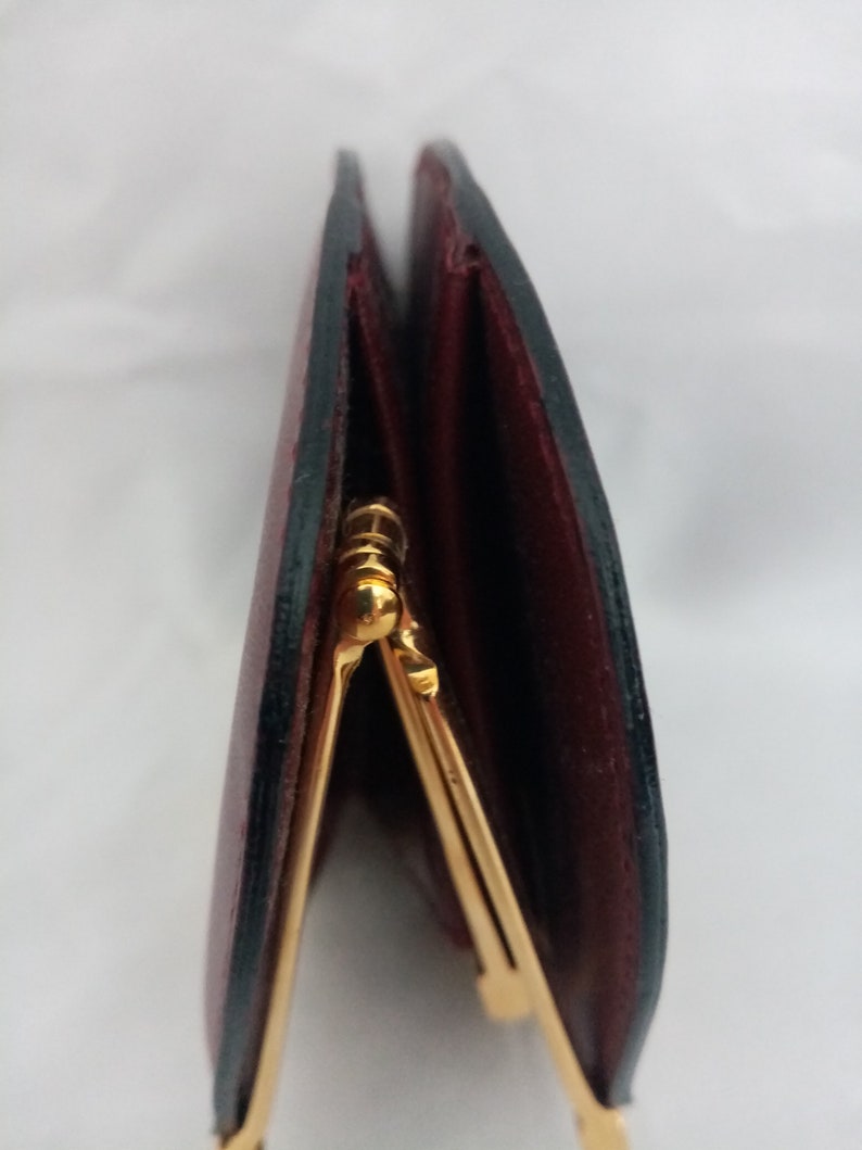 May include: A close-up of a burgundy leather wallet with a gold clasp. The wallet is folded in half and the clasp is visible in the center of the image.