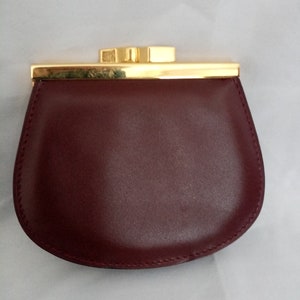 May include: A burgundy leather coin purse with a gold metal clasp and trim.