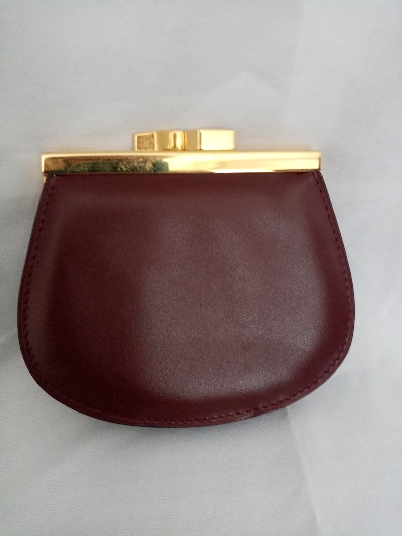 May include: A burgundy leather coin purse with a gold metal clasp and trim.