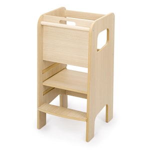 May include: A light-coloured wooden learning tower featuring a tall, enclosed frame with a horizontal safety bar at the top, a central platform, and a single lower step. The structure includes side cutouts for handles and a smooth, natural wood grain finish.