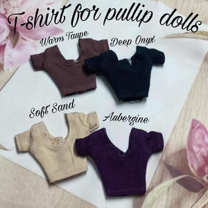 Op de afbeelding: Vier miniatuur T-shirts voor Pullip poppen in de kleuren Warm Taupe, Deep Onyx, Soft Sand en Aubergine. Elk shirt heeft een V-hals en korte mouwen. De tekst "T-shirt for pullip dolls" staat bovenaan.