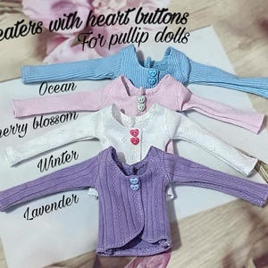 Puede incluir: Cuatro suéteres en miniatura para muñecas pullip en colores pastel: azul claro, rosa, blanco y lavanda. Cada suéter tiene botones en forma de corazón y está etiquetado con un nombre de color. El texto "Sweaters with heart buttons For pullip dolls" está en la parte superior.