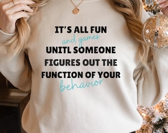 Puede incluir: Una sudadera blanca con el texto "It's all fun and games until someone figures out the function of your behavior" en negro y azul.