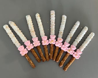 May include: A group of ten pretzel sticks dipped in white chocolate and decorated with gold sprinkles and pink bear-shaped sweets.