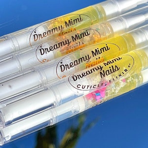 May include: Four clear tubes with yellow liquid and glitter inside. The tubes have labels that say "Dreamy Mimi Nails Cuticle Elixir".