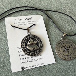May include: Two silver-toned circular pendants on black cords. One pendant features a wolf head relief surrounded by runes. The other displays a Vegvisir symbol encircled by runes and the text FOREVER IN THE LIFE. They rest on a white card with the text I Am Wolf, It is my nature to be kind, gentle and loving, Quiet, Silent, Patient, For I am a warrior, And I will Survive, and EnchantedCuriositys.