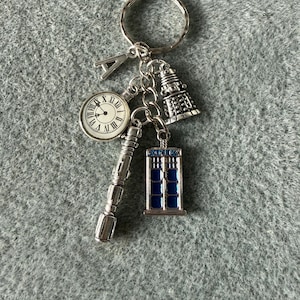 May include: Silver Doctor Who themed keychain with charms including a clock, a Dalek, a sonic screwdriver, and a blue police box. The keychain has a silver letter "A" charm and a large key ring.