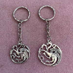 May include: Two silver keyrings with a dragon design. Each keyring features a circular pendant with a detailed dragon design.