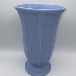 Op de afbeelding: Een lichtblauwe keramische vaas met een geribbeld ontwerp en een voet.
