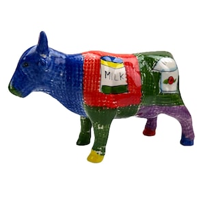 May include: A ceramic cow figurine with a patchwork design. The cow's head is blue, the body is divided into red, green, and purple sections. The red section has a milk carton illustration. The cow's legs are green, yellow, and red.