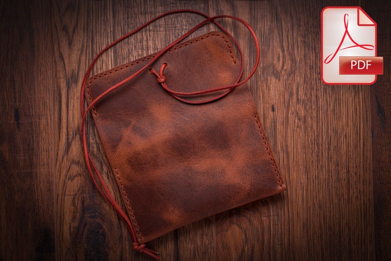 May include: A brown leather pouch with a red drawstring closure. The pouch is lying on a wooden surface.