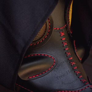 May include: A black leather mask with red stitching and a gold trim. The mask has a mesh covering the eyes and the text "Designed by Tree House Patterns" is embossed on the side.