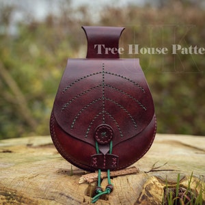 May include: A burgundy leather pouch with a green leaf design and a green drawstring. The pouch is sitting on a wooden surface. The text "Tree House Patterns" is visible in the background.