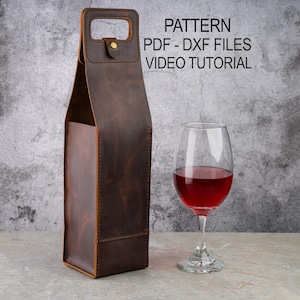 Könnte beinhalten: Eine braune Weinflaschentasche aus Leder mit Griff und goldfarbenem Knopfverschluss. Ein Weinglas mit Rotwein steht neben der Tasche. Der Text auf dem Bild lautet "PATTERN PDF - DXF FILES VIDEO TUTORIAL".
