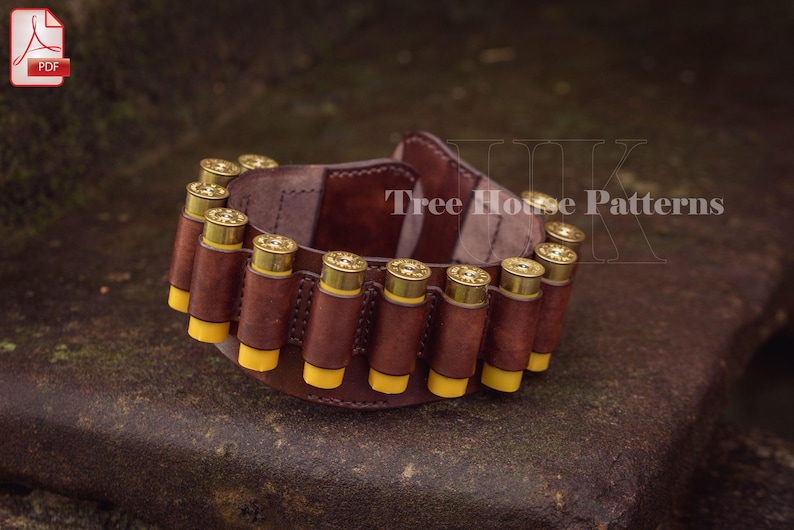 May include: A brown leather shotgun shell holder with 12 yellow shotgun shells. The holder is on a brown surface. The text 'Tree House Patterns' is visible on the holder.
