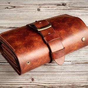 May include: A brown leather wallet with a buckle closure. The wallet is rolled up and has a distressed look.