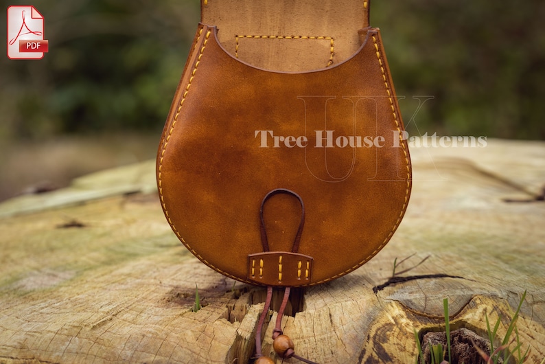 May include: A brown leather pouch with a yellow stitch detail and a brown leather strap. The pouch is sitting on a wooden surface.