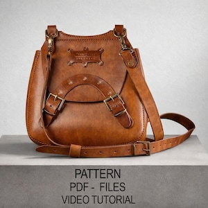 以下が含まれることがあります： 調節可能なストラップと金属製のバックルが付いた茶色の革製バッグ。 バッグには、2 つのバックルと装飾的なエンブレムが付いた湾曲したフラップが付いています。 下部には「PATTERN PDF - FILES VIDEO TUTORIAL」というテキストが表示されています。