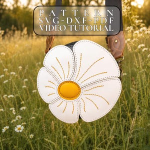 Peut inclure: Un sac à bandoulière blanc en forme de marguerite avec un centre jaune et des détails cousus. Le sac a un intérieur noir et une bandoulière en cuir marron. L'image comprend le texte "PATTERN SVG-DXF-PDF VIDEO TUTORIAL". Le sac est posé sur un fond d'herbes hautes et de fleurs sauvages.