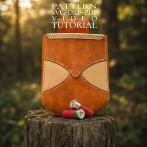 Peut inclure: Un sac à cartouches en cuir marron avec des accents beiges et des coutures décoratives. Deux cartouches de fusil rouges sont devant le sac. Le texte "PATTERN SVG-DXF-PDF VIDEO TUTORIAL" est en haut.